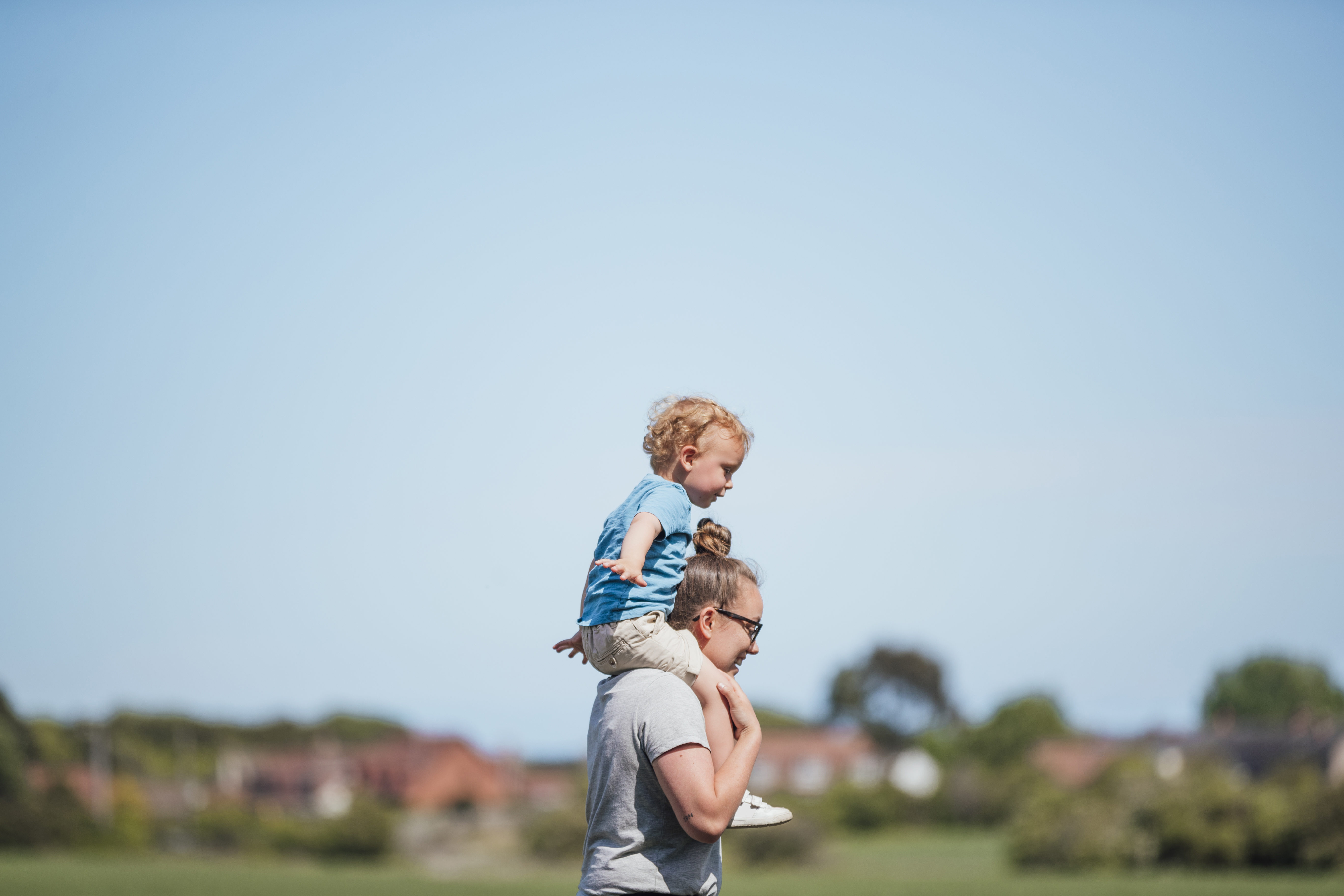 Small child on adult's shoulders against a blue sky